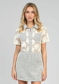 Blouse en dentelle à manches courtes et jupe grise texturée ; comporte deux poches poitrine et une fermeture à boutons ; motif en dentelle florale complexe.