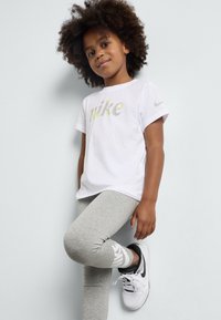 Camiseta blanca de manga corta con el logo de "nike", combinada con leggings grises y zapatillas en blanco y negro. Tejido suave, corte relajado.