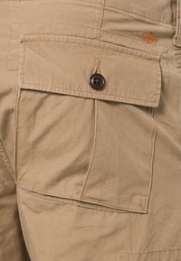 Beige cargoshorts met een groot klepzakje met een knoopsluiting en oranje stiksel. Gemaakt van een textuurrijke katoenen stof.