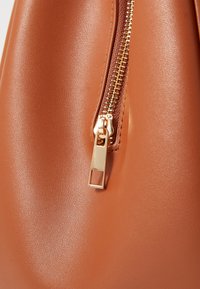 Sac à main en simili cuir marron avec une fermeture éclair dorée. La fermeture éclair est dotée d'une tirette rectangulaire et de détails texturés lisses.