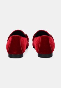 Zapatos de lona de terciopelo rojo con una textura suave, forma redondeada, suela negra y un ribete decorativo en la parte trasera. Sin hardware o acentos visibles.