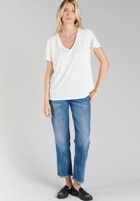 Witte V-hals T-shirt, losse pasvorm, gecombineerd met middelhoge blauwe jeans, lichtelijk verouderd bij de mouwen, en zwarte instappers. Eenvoudige en casual uitstraling.