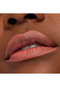 Matt leppestift i en varm nudefarge, som fremhever teksturerte lepper med synlige linjer og en naturlig glans i midten. Nærbilde.