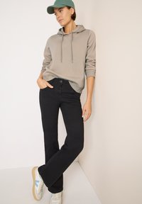 Černé rozšířené džíny s přiléhavým pasem, spárované se světle šedou mikinou s kapucí a odpovídající zelenou kšiltovkou; bílé tenisky.