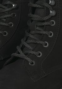 Las botas de cuero negro tienen cordones redondos, ojales de metal y una textura suave. El diseño es funcional con una suela resistente y costuras reforzadas.