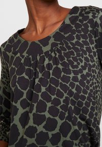Zwarte en groene blouse met een dierenprint patroon, ronde halslijn en geplooide details aan de voorkant. Zachte stof en driekwartmouwen.