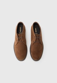 Brown suede shoes with a rounded toe, lace-up design, and a textured surface. Features a black rubber sole and "GEOX Respira" branding inside.