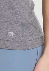 Graues sportliches Oberteil mit kurzem Ärmel, strukturierter Stoff und dezentem Logo; kombiniert mit blauen Leggings mit glatter Oberfläche.