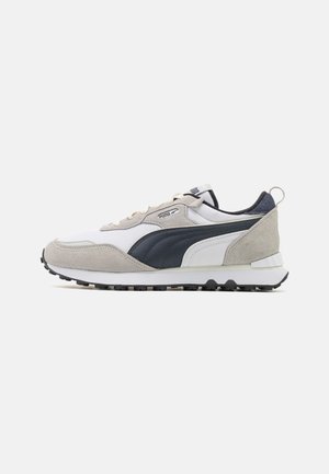 Zapatillas Puma con parte superior de malla blanca, acentos de cuero azul marino, detalles en gamuza gris y suela de goma negra. Presenta cordones y una lengüeta en el talón.
