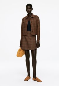Brown plaid jacket and skirt set with a fitted design, paired with a black top, tan suede loafers, and a yellow suede handbag.