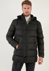 Piepūšamā melnā jaka ar kapuci, pilns priekšējais rāvējslēdzis un sānu kabatas. Satur horizontālu quilted rakstu un regulējamas auklas.