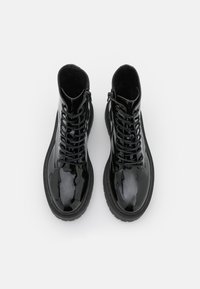 Bottes chevilles en cuir verni noir avec une finition lisse, design à lacets et semelles épaisses noires. Présente une fermeture éclair sur le côté.