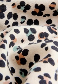 Tissu à motifs présentant un fond beige avec des taches noires, vertes et pêches. La texture semble douce et tricotée.