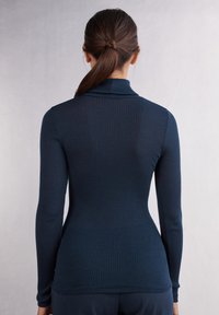 Námořnická modrá pruhovaná blůza s dlouhým rukávem a vysokým límcem. Přiléhavý silueta a texturovaná tkanina, která zajišťuje elegantní vzhled. Žádné viditelné logo nebo akcenty.