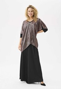 Shiny, metallic tunic top with wide sleeves, featuring a V-neck and a longer, curved hem. Paired with black, flowy pants and heels.
