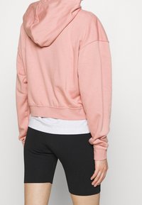 Rosa kort hoodie med dragsko i huvan, mjukt tyg, ribbade muddar, lagd över en vit t-shirt, tillsammans med svarta cykelshorts.
