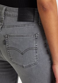 Pantalones vaqueros de mezclilla gris con un diseño ajustado, que presentan un bolsillo trasero delimitado por costuras y una etiqueta de cintura de cuero negro.