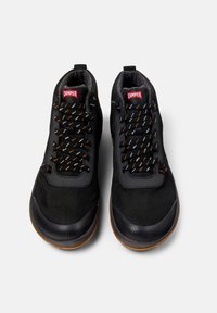 Zapatillas negras con una parte superior de tela texturizada, cordones contrastantes en naranja y blanco, cuello acolchado y suela de goma con un patrón texturizado.