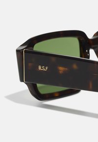 Occhiali da sole in tartaruga marrone con lenti verdi. Presentano una incisione dorata "R.S.F." sul lato e un audace design della montatura geometrica.