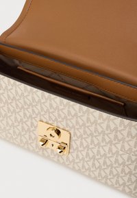 Μπεζ τσάντα χειρός με πατρόν, χρυσό μεταλλικό κούμπωμα και καφέ δερμάτινη επένδυση εσωτερικά. Διαθέτει λογότυπο σε πατρόν και λεπτομέρεια εσωτερικής τσέπης.