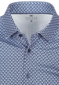 Dunkelblaue Button-Up-Bluse mit einem geometrischen hexagonalen Muster, aus leichtem Material gefertigt, mit einem Standardkragen und sichtbaren Knöpfen.