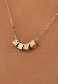 Gouden ketting met vierkante kralen met gegraveerde letters "I," "B," en "E," en een heldere edelsteenaccent. De ketting heeft een delicaat patroon.