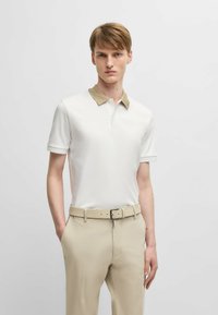 Polo bianco con colletto beige, maniche corte. Abbinato a pantaloni beige e una cintura coordinata. Design semplice, tessuto liscio.