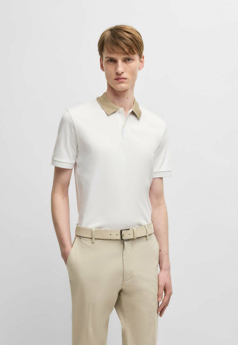 Polo bianco con colletto beige, maniche corte. Abbinato a pantaloni beige e una cintura coordinata. Design semplice, tessuto liscio.