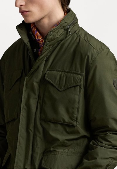 Olivgrüne gepolsterte Jacke mit zwei Brusttaschen, Reißverschluss und hohem Kragen. Glatte Textur mit leichtem Erscheinungsbild.