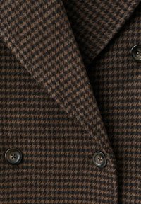 Manteau en laine marron et noir à motif pied-de-poule avec double boutonnage, larges revers et boutons ronds foncés.