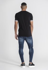 Camiseta negra con mangas cortas de cuadros, combinada con unos jeans ajustados azules desgastados y zapatos negros con un patrón blanco.