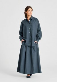 Dunkelblaues, übergroßes Hemd mit Knopfleiste und Brusttasche, kombiniert mit einem passenden langen Rock. Weicher, strukturierter Stoff mit lockerer Passform.