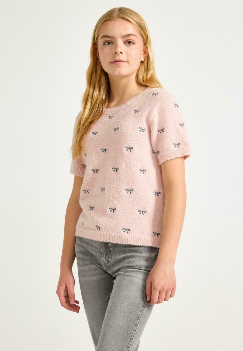 Lyserød kortærmet sweater med en blød tekstur, der har små sorte sløjfemønstre over det hele og en rund halsudskæring.