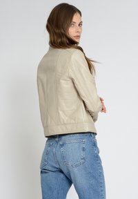Beige Lederjacke mit taillierter Passform, sichtbaren Nähten und Schultersehen. Kombiniert mit hellblauen hoch taillierten Denim-Jeans.