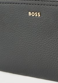 Must nahast rahakott kuldse "BOSS" logoga. Omab nähtavaid õmblusi ja siledat pinda, mis viitab kvaliteetsele käsitööle.