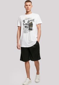 Hvit t-skjorte med kort erme som har et tegneserieaktig grafikk med en boks og tekst, sammen med svarte treningsshorts og hvite sneakers.