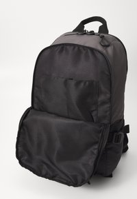 Sac à dos en nylon noir avec une texture lisse, fermetures éclair, poche frontale plate, bretelles ajustables et une poignée supérieure pour le transport.