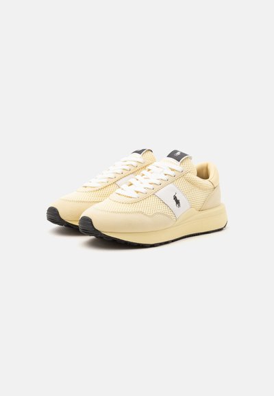 Paire de baskets en mesh beige et blanc avec des lacets blancs et un logo noir sur le côté et la languette, affichée sur fond blanc.