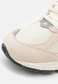 Beigefarbener Wildleder- und Mesh-Sneaker mit grauen Akzenten, einer strukturierten Oberfläche, abgerundeter Form und einer schwarzen Gummisohle.