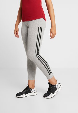 Leggings grigi con strisce verticali nere sui lati, abbinati a scarpe da ginnastica bianche e nere. Indossati con una canotta rossa.