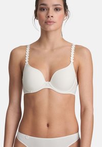 Sostén blanco con copas contorneadas, tirantes texturizados con borde en picos y un detalle de botón en el centro. Tela suave con un diseño minimalista.