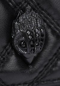 Primo piano di una borsa a tracolla in pelle nera con un pezzo di hardware decorativo a forma di mano, ricco di dettagli ornamentali e pietre nere.