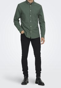 Groene overhemd met knopensluiting en een borstzak, gecombineerd met zwarte slim-fit jeans en zwarte enkelboots, met een zachte katoenstructuur.