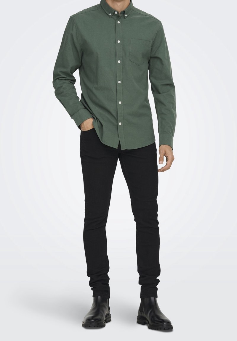 Groene overhemd met knopensluiting en een borstzak, gecombineerd met zwarte slim-fit jeans en zwarte enkelboots, met een zachte katoenstructuur.