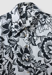 Blusa floreale in bianco e nero con colletto e chiusura a bottoni. Tessuto liscio caratterizzato da grandi fiori e foglie in vari motivi.