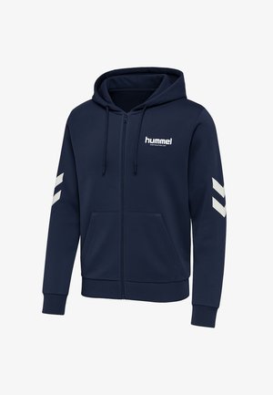 Marinblå zip-up hoodie av mjukt tyg med en framstående logotyp, två sidfickor och vita chevron-accenter på ärmarna. Huvan har snören.