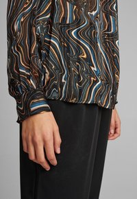 Blusa nera e multicolore con motivo vorticoso blu, marrone e bianco, con maniche lunghe e polsini con bottone.