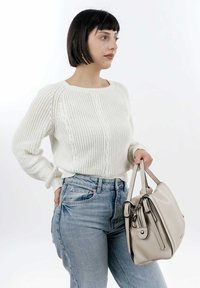 Cream knit sweater with cable design, paired with high-waisted distressed blue denim jeans. Holding a light beige handbag with hardware accents.