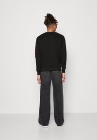 Sudadera negra de manga larga, con cuello redondo y puños de canalé, combinada con jeans de pierna ancha en gris oscuro y zapatillas blancas.
