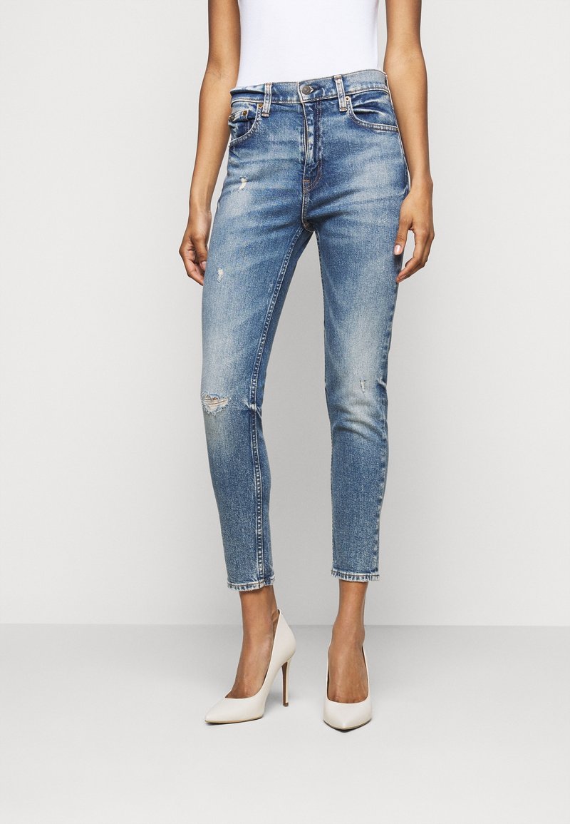 Lichtblauwe spijkerbroek met een slim fit ontwerp, voorzien van lichte slijtage, vijf zakken en een cropped lengte. Draagt met crèmekleurige hoge hakken.